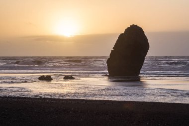 Gold Beach Oregon 'da gün batımı sahnesi. Renkli bulutlar ve dalgalar ıslak kum ve kayalara yansıyan renkler ekliyor.