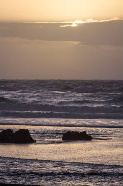 Gold Beach Oregon 'da gün batımı sahnesi. Renkli bulutlar ve dalgalar ıslak kum ve kayalara yansıyan renkler ekliyor.
