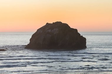 Bandon 'da deniz kıyısındaki insan yüzüne benzeyen bir kayanın yakınında batan güneşten gelen turuncu gökyüzü.