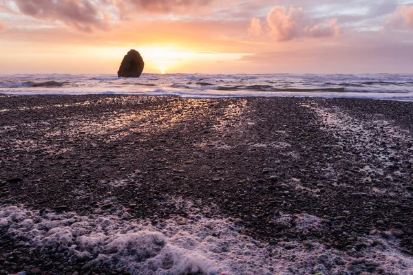 Gold Beach Oregon 'da gün batımı sahnesi. Renkli bulutlar ve dalgalar ıslak kum ve kayalara yansıyan renkler ekliyor.