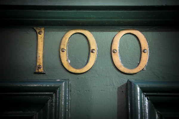 Number one hundred brass door number on weathered painted doorway — Stock Photo, Image