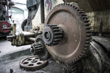 Terk edilmiş fabrikada paslı dişliler ve makineler.