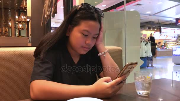 Moody дівчина сидить за столом в кафе за допомогою мобільного телефону в очікуванні її харчування — стокове відео