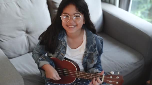 Retrato de niña atractiva, con gafas y chaqueta de jean, escuchando música con auriculares en la sala de estar — Vídeos de Stock