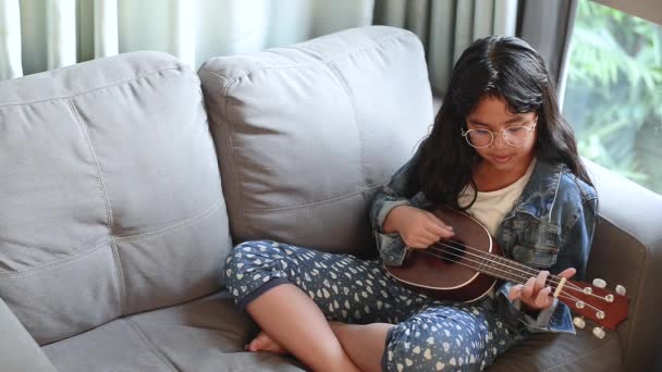 Портрет молодой привлекательной девушки в очках и джинсовой куртке, слушающей музыку с наушниками в гостиной — стоковое видео