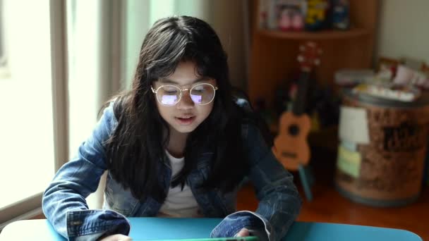Портрет молодой привлекательной девушки в очках и джинсовой куртке, слушающей музыку с наушниками в гостиной — стоковое видео