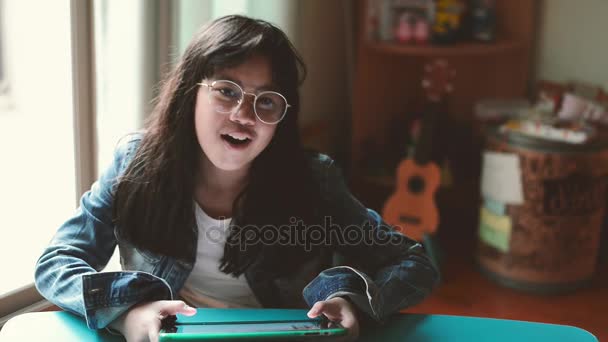 Retrato de niña atractiva, con gafas y chaqueta de jean, escuchando música con auriculares en la sala de estar — Vídeo de stock