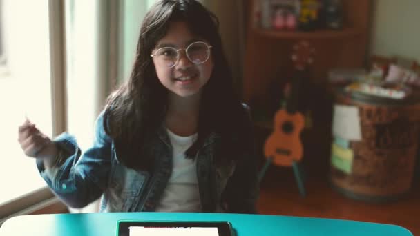 Porträtt av ung attraktiv flicka, bär glasögon och jeansjacka, lyssna på musik med hörlurar i vardagsrummet — Stockvideo