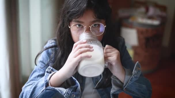 Retrato de una chica sonriente escuchando música y bebiendo leche en el salón. Mustache de leche — Vídeos de Stock