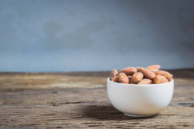 Ahşap masa üzerinde beyaz kase içinde tuz kavrulmuş badem