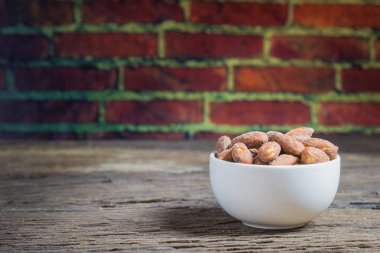 Ahşap masa üzerinde beyaz kase içinde tuz kavrulmuş badem