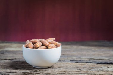 Ahşap masa üzerinde beyaz kase içinde tuz kavrulmuş badem