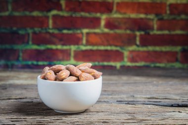 Ahşap masa üzerinde beyaz kase içinde tuz kavrulmuş badem