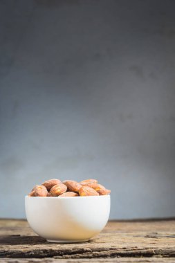Ahşap masa üzerinde beyaz kase içinde tuz kavrulmuş badem