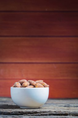 Ahşap masa üzerinde beyaz kase içinde tuz kavrulmuş badem