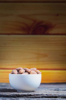 Ahşap masa üzerinde beyaz kase içinde tuz kavrulmuş badem