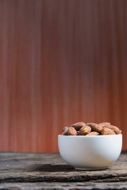 Ahşap masa üzerinde beyaz kase içinde tuz kavrulmuş badem