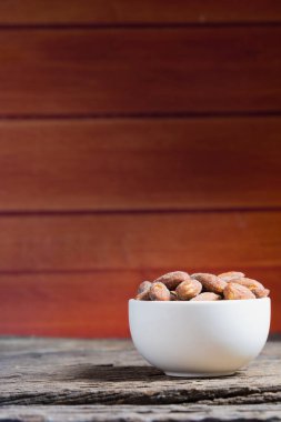Ahşap masa üzerinde beyaz kase içinde tuz kavrulmuş badem