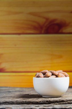 Ahşap masa üzerinde beyaz kase içinde tuz kavrulmuş badem