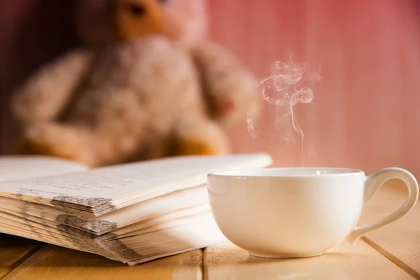 Taza de café y libro centrado en el oso de peluche en fondo borroso —  Fotos de Stock