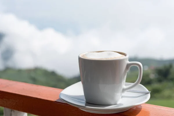 Close up white cup of hot coffee on balcony edge with outdoor na