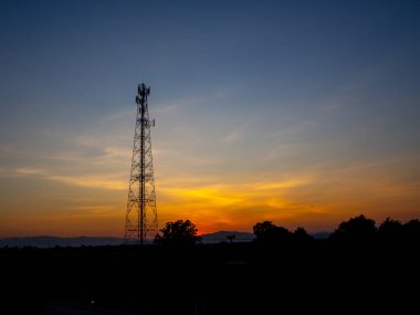 Alacakaranlık gökyüzünün altındaki cep telefonu anteninin silueti. Şafak vakti gökyüzünde güzel bulutlarla iletişim anten kulesi