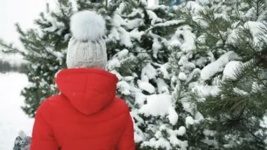 Güzel kadın neşeyle iğne yapraklı ağaçlar tarafından kar kaplı yürür.