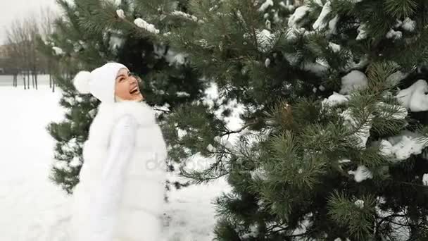 Jovem mulher girando em roupas brancas de inverno perto de um grande pinheiro — Vídeo de Stock