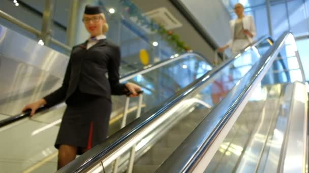 Flight attendant and passengers with suitcases down escalator — Stock Video