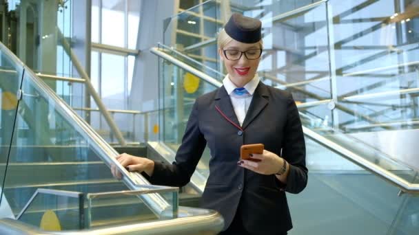 Flygvärdinna med glasögon läser ett meddelande på telefonen och ler. — Stockvideo
