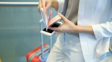Beyaz elbiseli yolcu belgili tanımlık evrak ve bir telefon tutarak denetler.