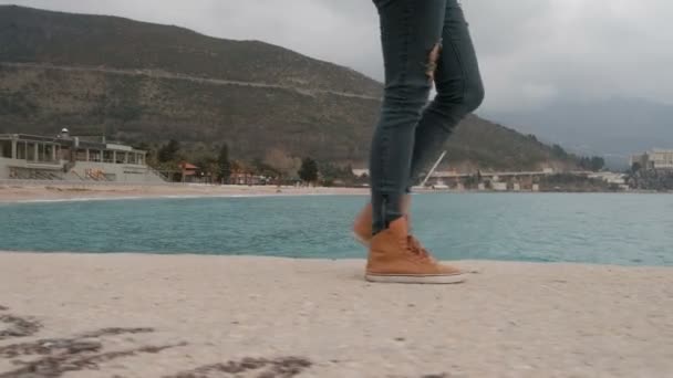 Människa i trasiga jeans och orange sneakers är sand kust. — Stockvideo