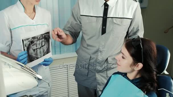El dentista discute con su paciente la radiografía, que la enfermera sostiene . — Vídeo de stock