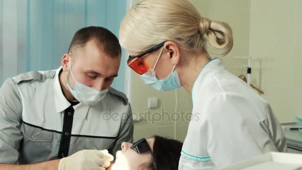 Стоматолог со своей симпатичной ассистенткой заполняет зуб пациенту в стоматологическом кабинете . — стоковое видео