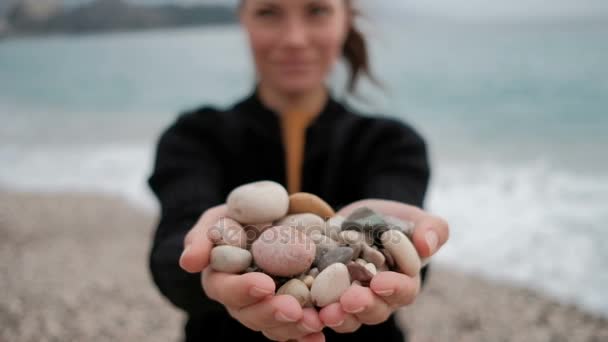 Woman holds in her hands a pile of rocks at the shore with the waves. — Stock Video