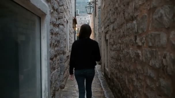 Disparando desde detrás de la mujer caminando en la calle estrecha en el casco antiguo — Vídeo de stock