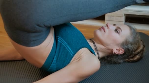 Тонка жінка лежить практикуючи йогу і отримує ноги за голову . — стокове відео