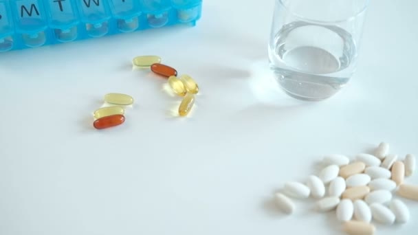 Auf dem Tisch liegen eine blaue Tablettenschachtel, gelbe Kapseln und ein Glas Wasser. — Stockvideo