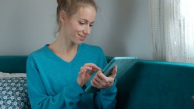Bir kadını mutlu kanepede otururken bir tablet üzerinde çalışıyor.