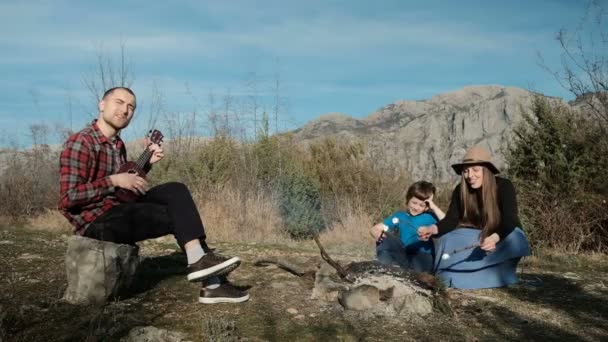 Une famille de trois personnes chante des chansons au coin du feu et fait frire une collation . — Video