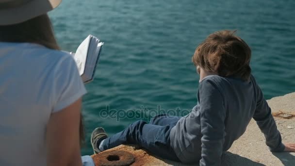 Anya elolvassa a könyvet, hogy fia, természeti tájat szabadban tenger mellett — Stock videók