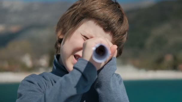 El niño sostiene la hoja retorcida como un telescopio y mira a través de ella . — Vídeos de Stock