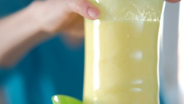 Uma mulher pressiona um possível liquidificador para fazer um smoothie amarelo . — Vídeo de Stock