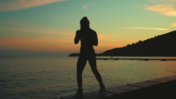 Silueta de mujer delgada joven que tiene entrenamiento de boxeo cerca del mar en la puesta del sol . — Vídeo de stock