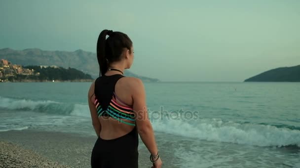 Женщина, идущая по берегу моря горы на заднем плане, глядя — стоковое видео