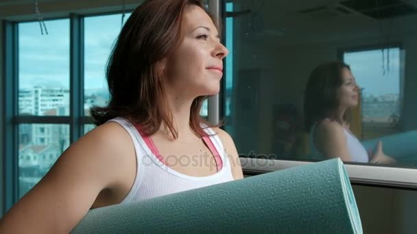 Een volwassen vrouw houdt een gevouwen yoga mat aan het einde van de training. — Stockvideo
