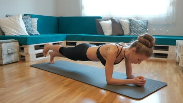 Νεαρή γυναίκα σε αθλητικά είδη κάνει άσκηση σανίδα στο πάτωμα σε εσωτερικούς χώρους. — Αρχείο Βίντεο