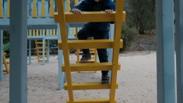 Menino sobe escadas no parque infantil ao ar livre . — Vídeo de Stock