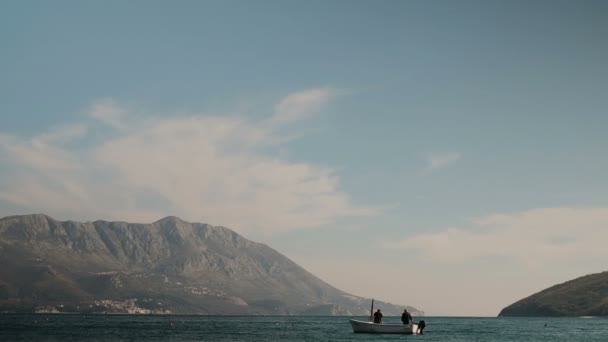 Kleine vissersboot op blauwe water van het meer omgeven door bergen. — Stockvideo