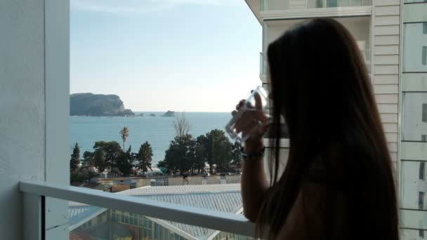 Jeune femme debout sur le balcon et l'eau potable à l'extérieur . — Video